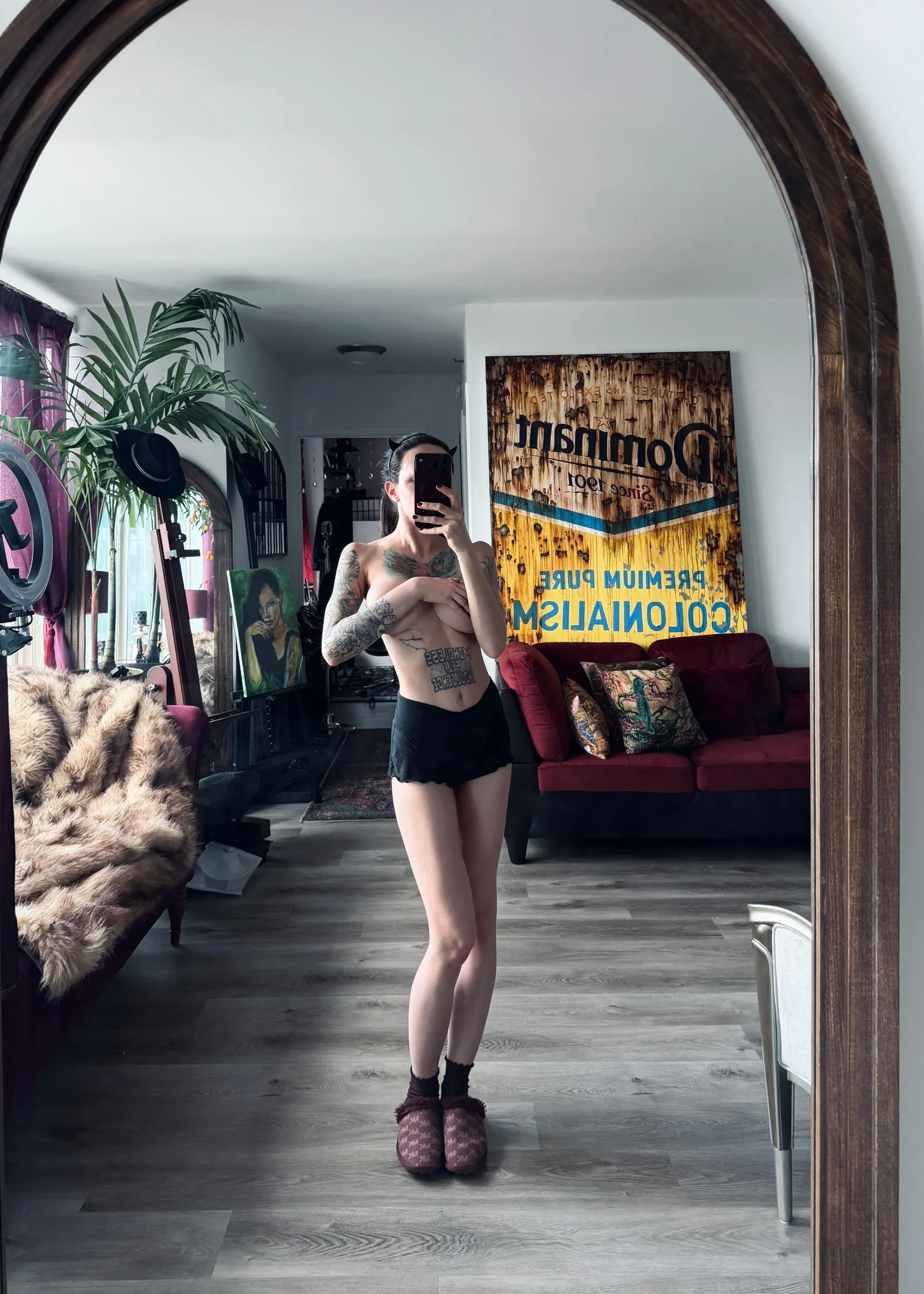 Iren Axel photographed in a mirror in her studio, the Dominant painting hanging on the wall behind her